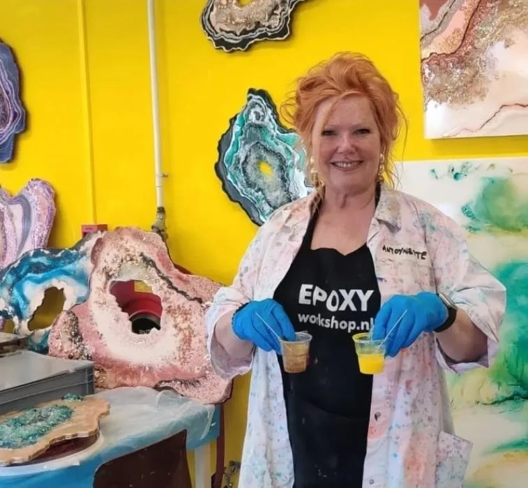 Antoynette Anema laughing in her studio, holding two cups of coloured epoxy